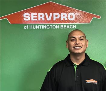 Male employee with buzzed hair hair smiling in front of a green background.