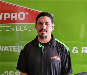 Male employee with spiky black hair smiling in front of a green truck.